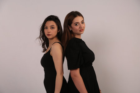 Two beautiful young women in black dresses on a white background in the studioの写真素材