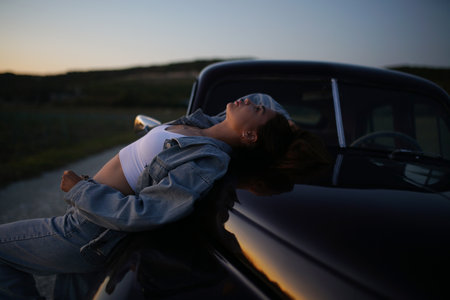Young woman sleeping on the hood of an old car at sunset.の写真素材