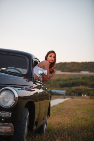 Beautiful young woman standing near a retro car on the road.の写真素材