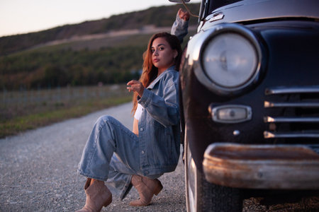 Young woman sitting on the road near her old car and holding a keyの写真素材