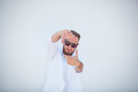 Handsome young man in traditional clothes and sunglasses making a frame with his handsの写真素材