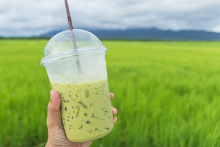 Hand holding a cup of milk greentea at the rice fieldの写真素材