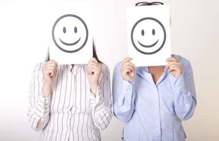 Portrait of a two young beautiful women holding smiley faces.の写真素材