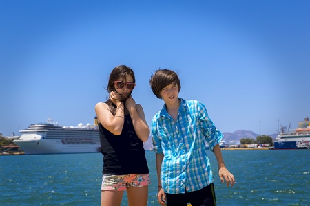 boy and girl teenager on travel, ocean and big ships in background.の写真素材