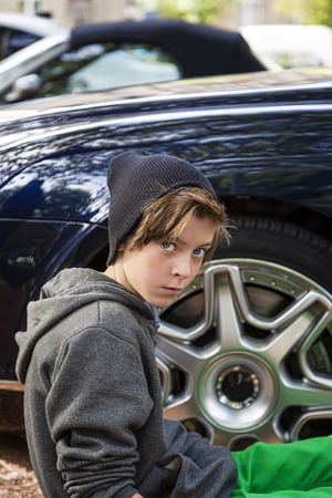 cool teenage boy sitting in front of a rim of wheel.の写真素材