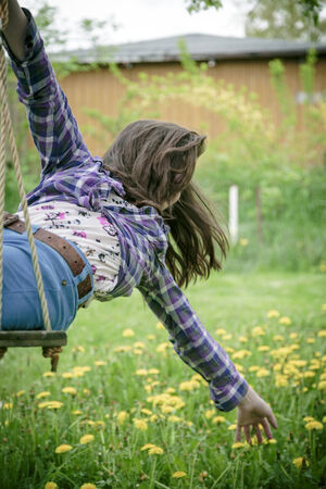 girl on a swing stretching here arm to a meadow.の写真素材