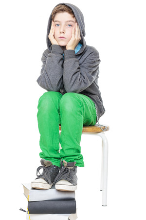 teenager boy sitting on a stool with his feet on a stack of books, isolated on white.の写真素材