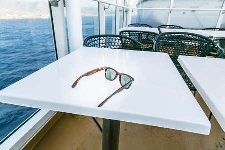 sunglasses laying on a white table with the ocean in background.の写真素材
