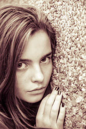 portrait of a female teenager leaning here face on a wall, with sepia color filter.