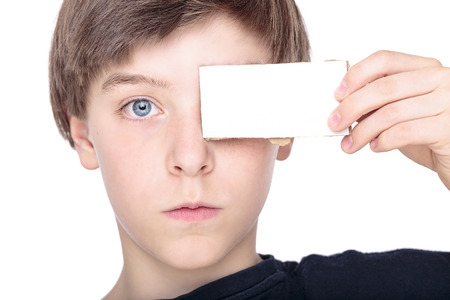 portait of a teenage boy holding a white piece of cardboard in front of one eye.の写真素材