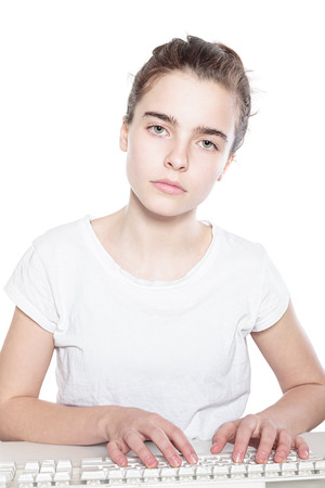 serious teenager girl working on a keyboard, isolated on whiteの写真素材