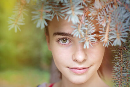 portrait of a smiling girl looking through blurred fir needles.