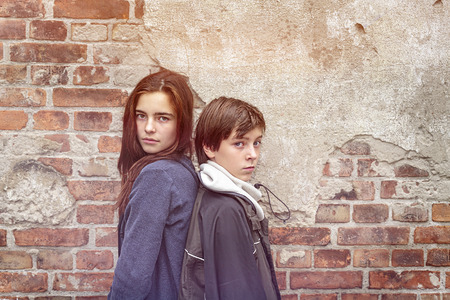 siblings back to back in front of an old brick wallの写真素材
