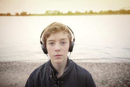 portrait of a teenage boy with headphones at a riverbank, toned imageの写真素材