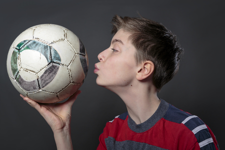 funny teenage boy is kissing a soccer ball, with gray background for fast isolatingの写真素材