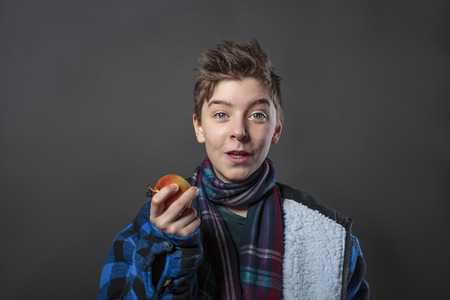 funny teenage boy holding an apple, isolated on gray backgroundの写真素材