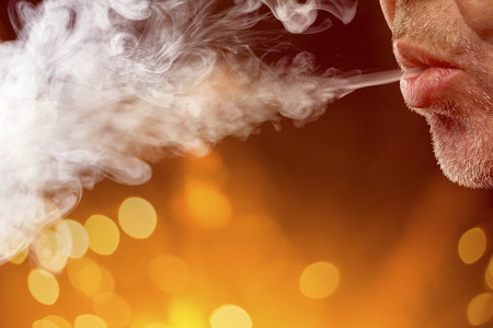 male mouth is blowing smoke out, with bokeh backgroundの写真素材