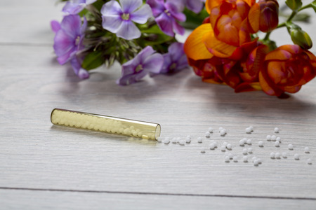 small glass tube with homeopathy globules  and flowers