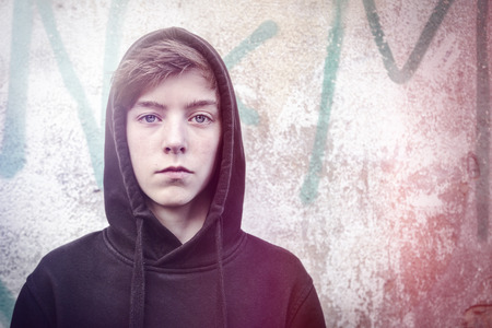 portrait of a teenage boy with black hoodie in front of a graffitiの写真素材