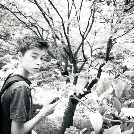 portrait of a teenage boy in a garden with smart phoneの写真素材