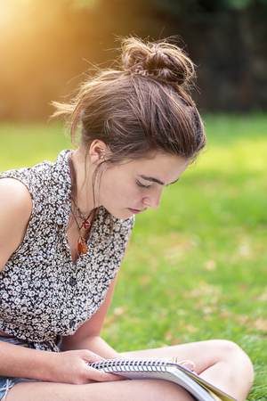teenage girl is sitting on a meadow and writingの写真素材