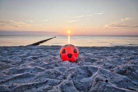 orange plastic soccer ball at the beach with sunsetの写真素材