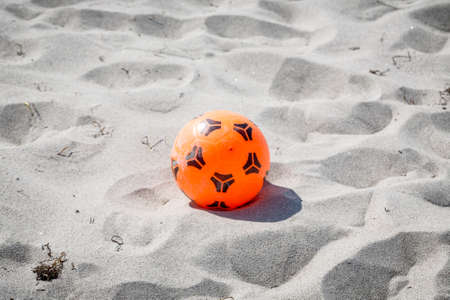 orange plastic soccer ball laying at the beach