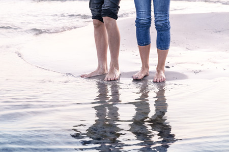 the legs of tow people reflected in the ocean