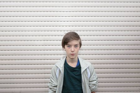 portrait of a boy with gray roller shutter in backgroundの写真素材
