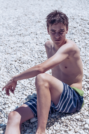 Portrait of a young man sitting at a stone beachの写真素材