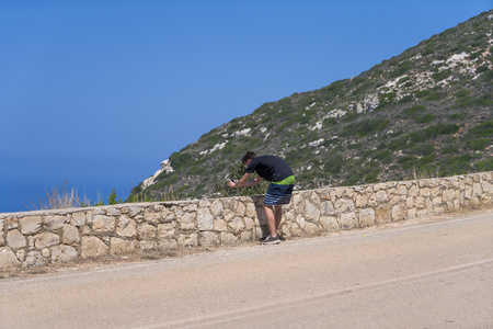 young man taking pictures with a phone in mediterranean landscapeの写真素材