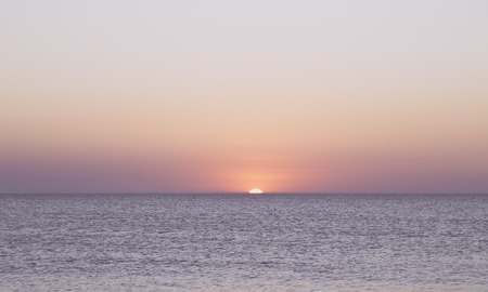 sunset over the horizon of the ocean with cloudless skyの写真素材