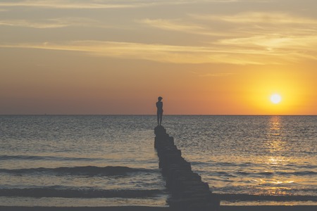 sunset over the baltic sea, young man is balancing on a groinの写真素材