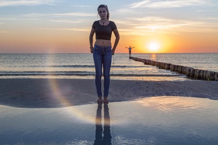 sunset over the baltic sea, portrait of a young woman standing on the beachの写真素材