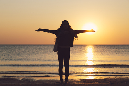 silhouette of a woman on a beach with stretched arms, setting sun on her handの写真素材