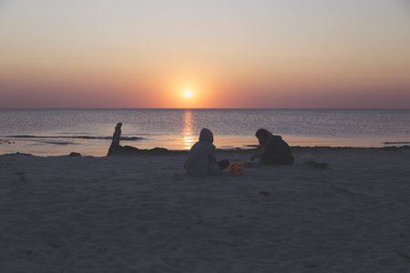 sunset over the sea, tow teens sitting on the beachの写真素材