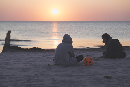 sunset over the sea, tow teens sitting on the beachの写真素材