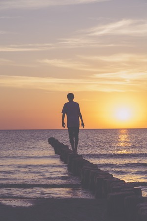 sunset over the baltic sea, young man is balancing on a groinの写真素材