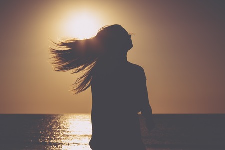 sunset on a beach, silhouette of a woman with flying hairの写真素材