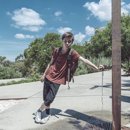 teen boy with backpack leaning on a faucet in a parkの写真素材