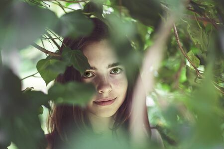 portrait of a young smiling woman covered of blurred leavesの写真素材