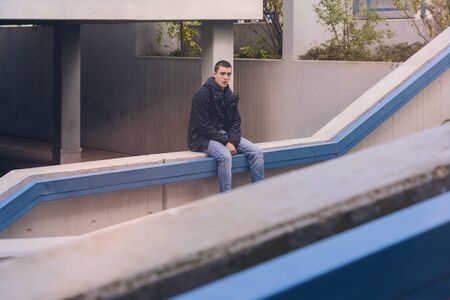 portrait of a casual young man in sitting on a concrete wall
