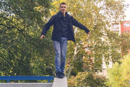 Smiling young man is balancing on a concrete wall