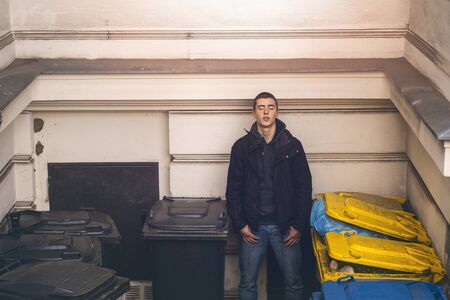 Portrait of a casual young man with closed eyes standing between garbage cansの写真素材