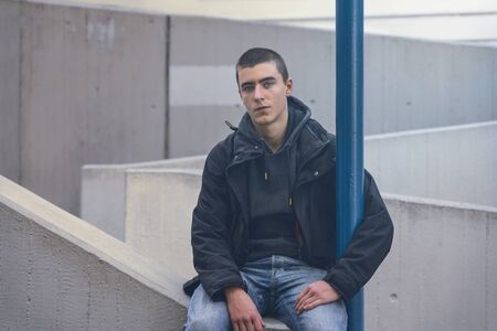 portrait of a casual young man in sitting on a concrete wallの写真素材