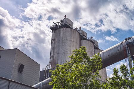three silos and a large pipe of a factory with dramatic sky