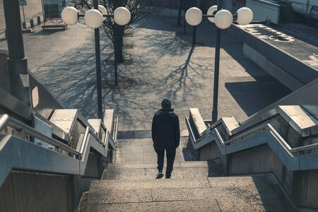 young man in black dress walks down a staircase in desolate surroundingsの写真素材