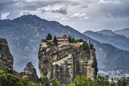 Monastery on a huge rock in Meteora, Greece with mountain range and dramatic cloudsの写真素材