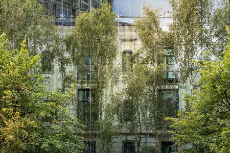 old house behind a modern glass facade with trees in foreground
