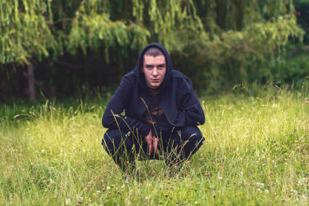 Portrait of a smiling, crouching man in a black hoodieの写真素材